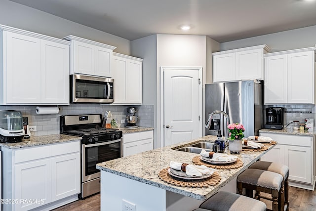 kitchen featuring white cabinets, appliances with stainless steel finishes, a sink, a breakfast bar area, and dark wood finished floors