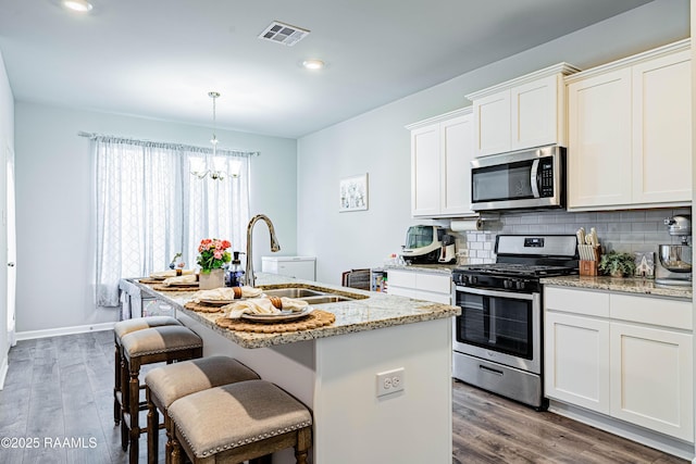 kitchen with an inviting chandelier, a sink, a kitchen island with sink, stainless steel appliances, and visible vents