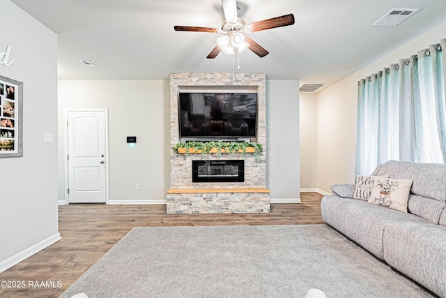 living room featuring ceiling fan, visible vents, a stone fireplace, and wood finished floors
