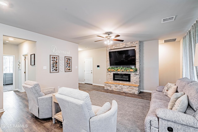 living area with a ceiling fan, dark wood finished floors, a stone fireplace, and visible vents