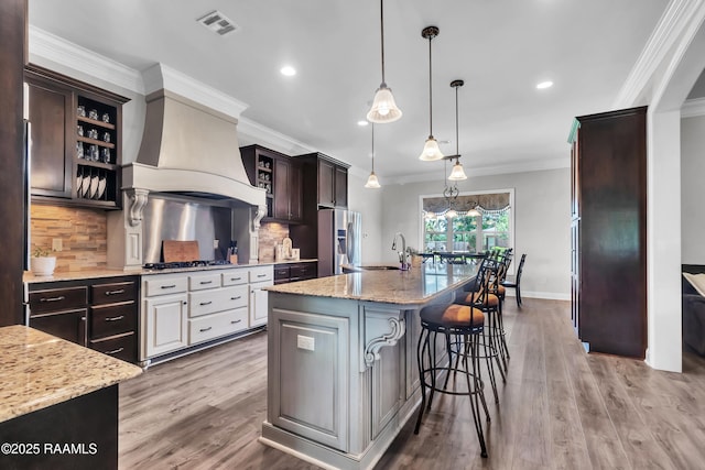 kitchen featuring visible vents, appliances with stainless steel finishes, dark brown cabinets, a sink, and ornamental molding