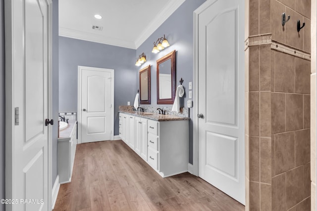bathroom featuring crown molding, double vanity, a garden tub, wood finished floors, and a sink