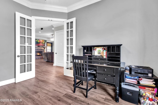 office area featuring a ceiling fan, french doors, wood finished floors, a warm lit fireplace, and ornamental molding