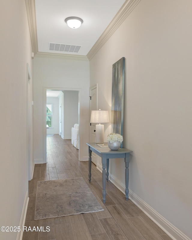corridor featuring baseboards, ornamental molding, wood finished floors, and visible vents