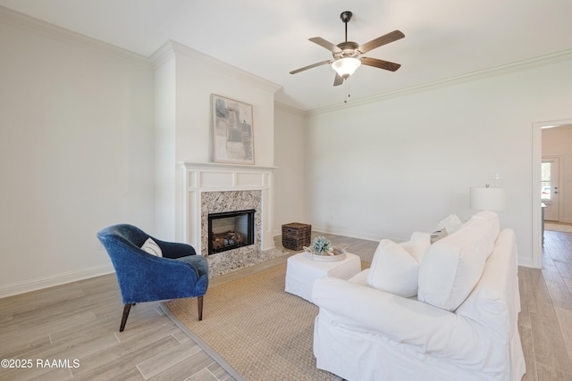 living area featuring a ceiling fan, ornamental molding, light wood finished floors, and a fireplace