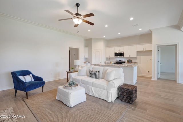 living room featuring crown molding, baseboards, ceiling fan, and light wood-style floors