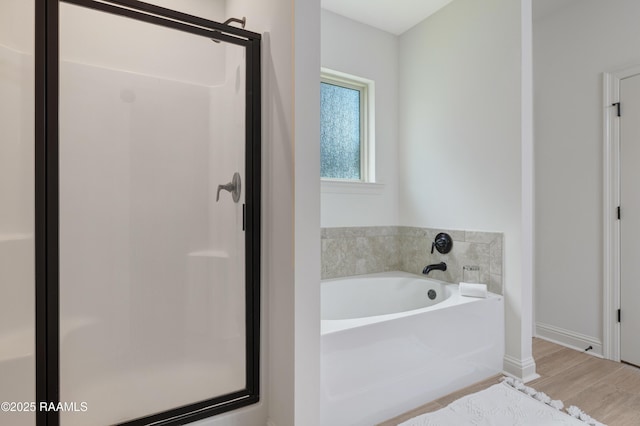 full bathroom with baseboards, a shower stall, a garden tub, and wood finished floors