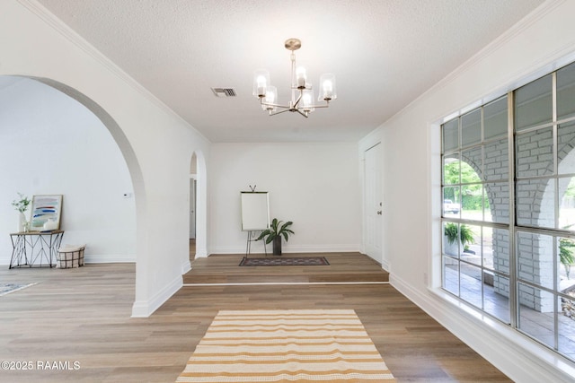 entrance foyer featuring a chandelier, ornamental molding, visible vents, and arched walkways