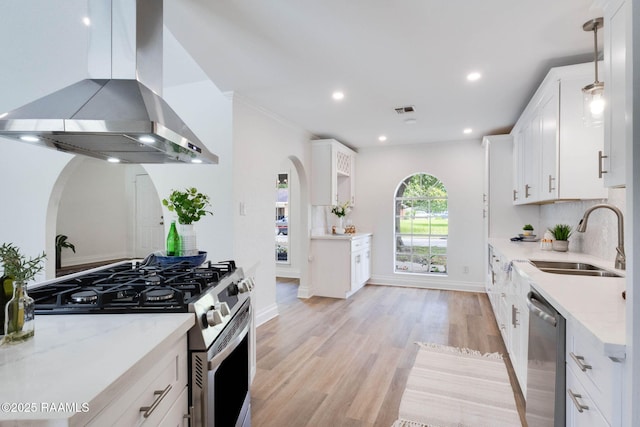 kitchen with a sink, island exhaust hood, arched walkways, stainless steel appliances, and white cabinets