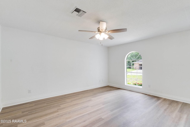 spare room with baseboards, ceiling fan, light wood-style flooring, and visible vents