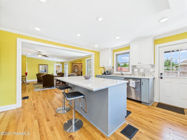 kitchen featuring a sink, a kitchen breakfast bar, stainless steel dishwasher, visible vents, and a kitchen island