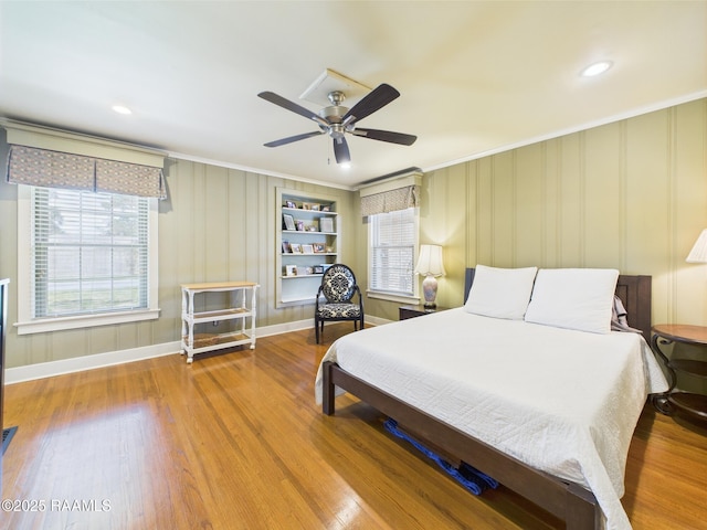 bedroom with crown molding, baseboards, a decorative wall, and wood finished floors