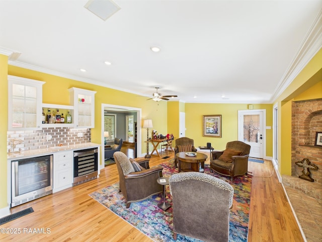 living area featuring wine cooler, ornamental molding, a ceiling fan, and wet bar