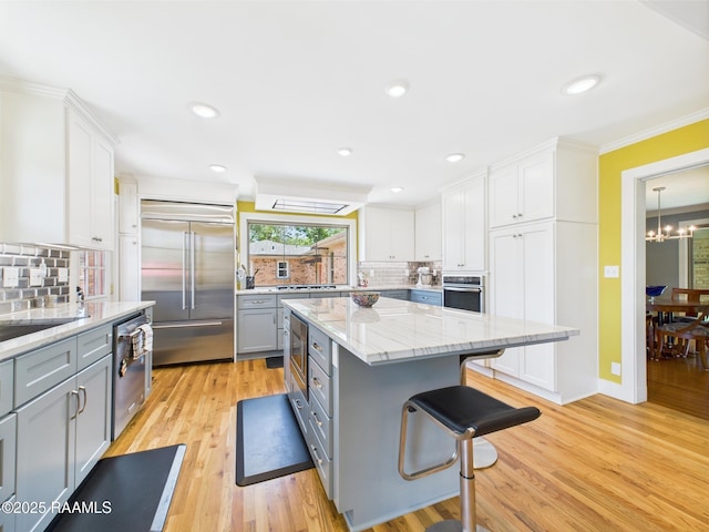 kitchen featuring gray cabinets, built in appliances, a breakfast bar, and tasteful backsplash