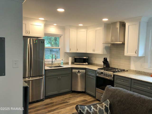 kitchen with gray cabinets, appliances with stainless steel finishes, a sink, white cabinets, and wall chimney exhaust hood