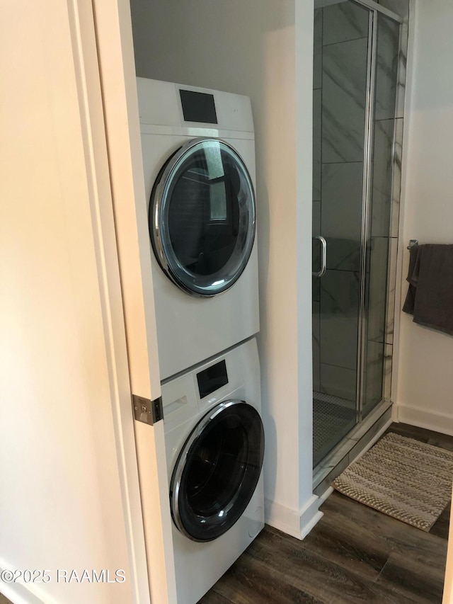 clothes washing area featuring baseboards, stacked washer and clothes dryer, dark wood finished floors, and laundry area