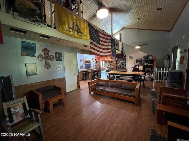 living area with a ceiling fan, high vaulted ceiling, wood finished floors, and a wainscoted wall