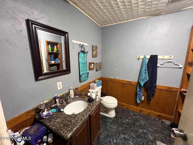 half bath with wooden walls, wainscoting, vanity, toilet, and ornamental molding