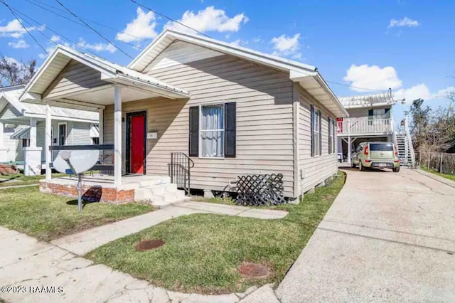 bungalow-style home featuring stairs, a front lawn, covered porch, and concrete driveway