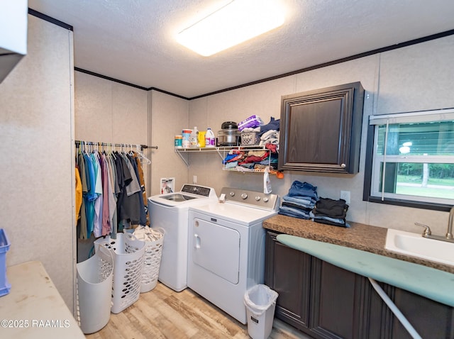 laundry area with a textured ceiling, a sink, washing machine and clothes dryer, light wood-style floors, and cabinet space