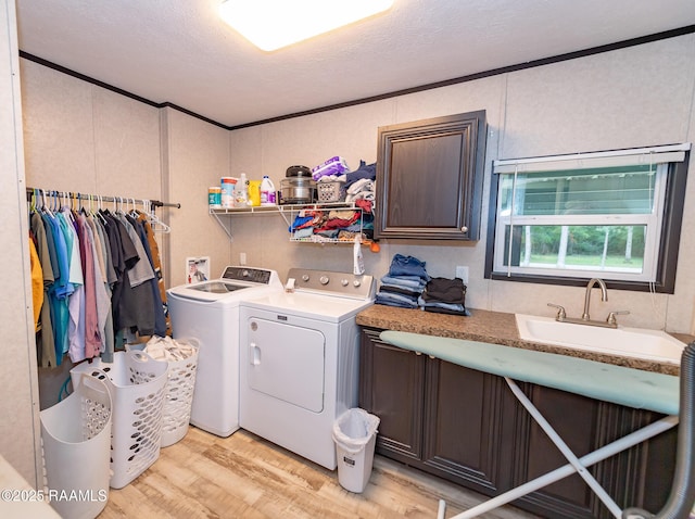 washroom with light wood finished floors, a sink, cabinet space, separate washer and dryer, and a textured ceiling