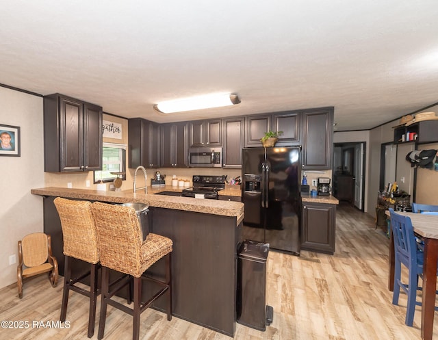 kitchen with a peninsula, a breakfast bar area, light wood-type flooring, black appliances, and light countertops