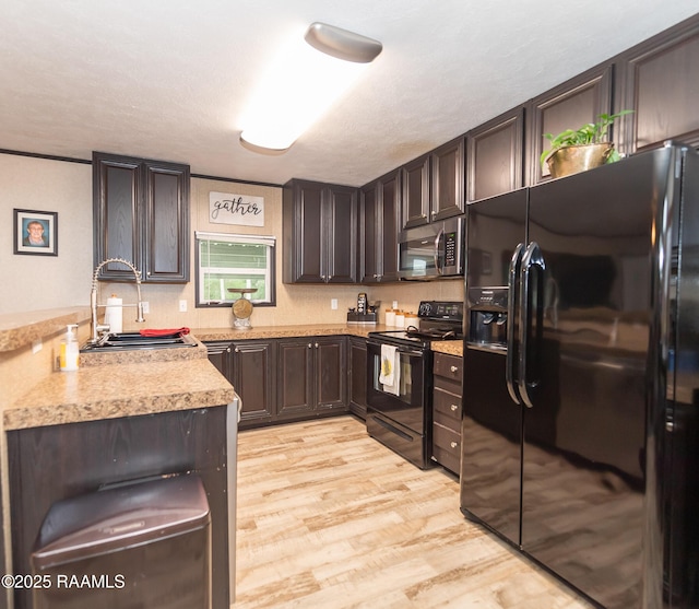 kitchen with dark brown cabinets, a sink, light wood-type flooring, black appliances, and light countertops
