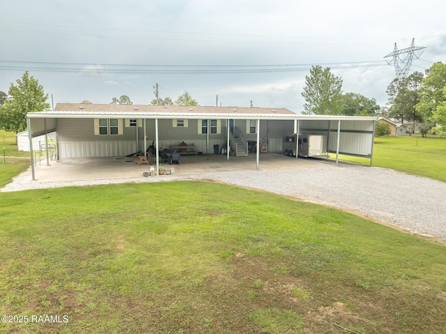 back of property featuring entry steps, a carport, gravel driveway, and a lawn