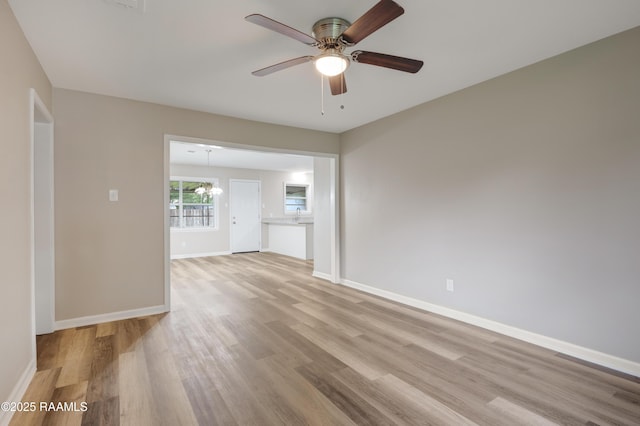 spare room with baseboards, light wood-style flooring, and ceiling fan with notable chandelier