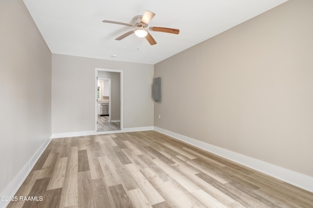 spare room featuring baseboards, ceiling fan, light wood-style flooring, and electric panel