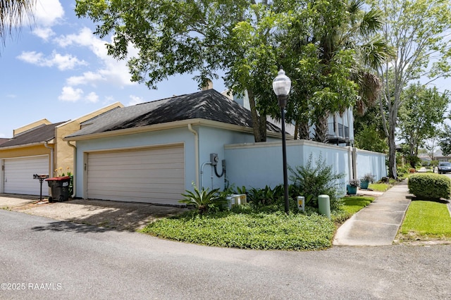 211 Ursuline St, Lafayette, LA 70506 - view of side of property featuring stucco siding, a chimney, a shingled roof, and an attached garage