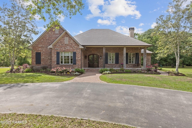 view of front of house featuring french doors, brick siding, a chimney, and a front yard