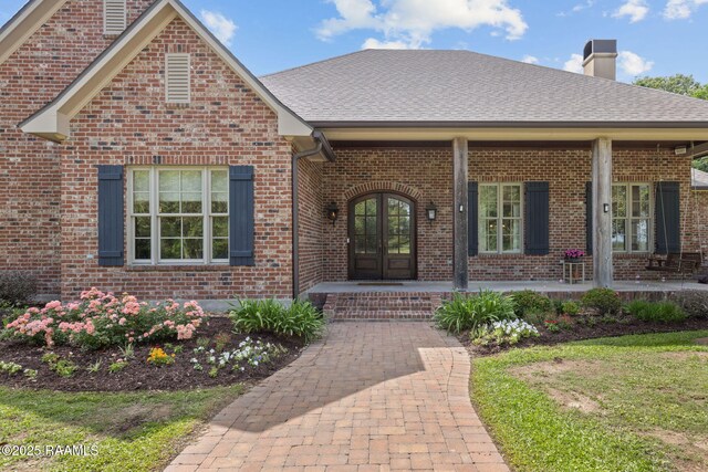 view of front facade with brick siding, roof with shingles, french doors, and a chimney