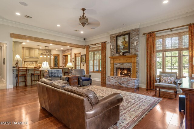 living area with a brick fireplace, ceiling fan, crown molding, and hardwood / wood-style floors