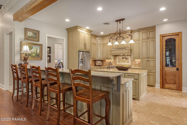 kitchen with cream cabinets, decorative backsplash, an island with sink, and stainless steel fridge with ice dispenser