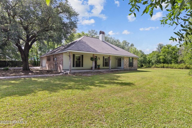 back of property featuring a porch, a chimney, brick siding, a yard, and an attached garage