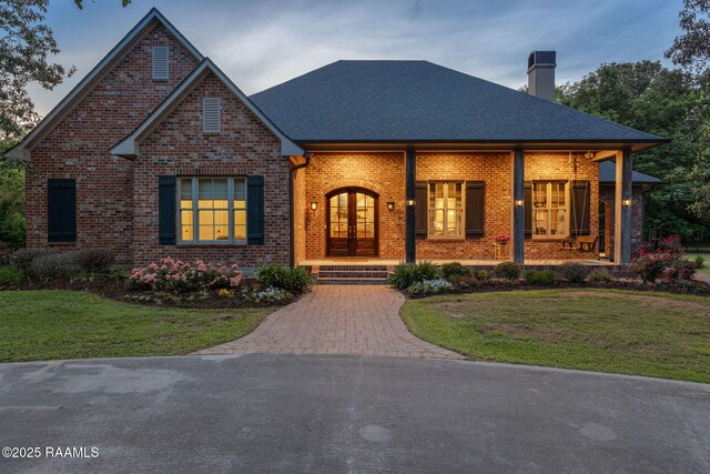 view of front of house featuring a front lawn, french doors, a chimney, brick siding, and a porch