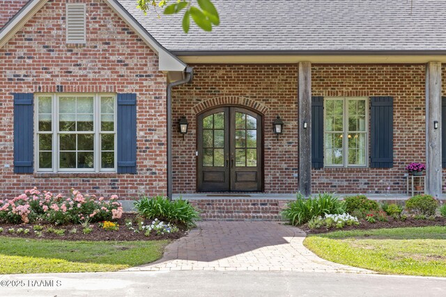 view of exterior entry with roof with shingles, french doors, and brick siding