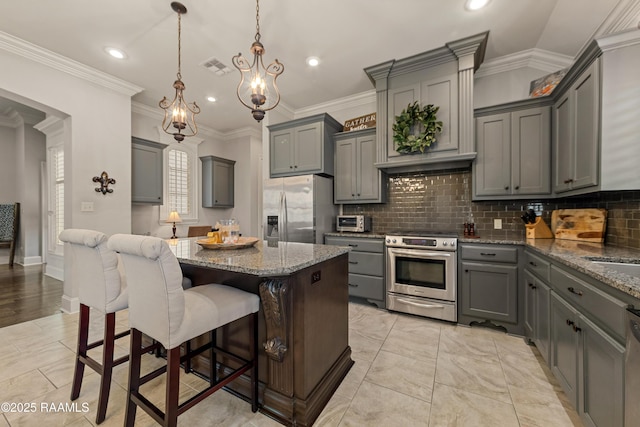 kitchen featuring light stone countertops, appliances with stainless steel finishes, a chandelier, gray cabinets, and decorative backsplash