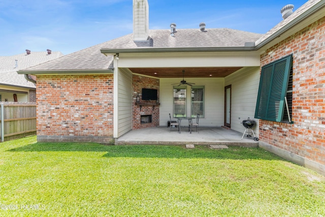 rear view of property with fence, brick siding, a patio area, a lawn, and a ceiling fan