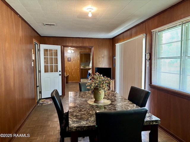 dining space featuring visible vents, wood walls, baseboards, and ornamental molding