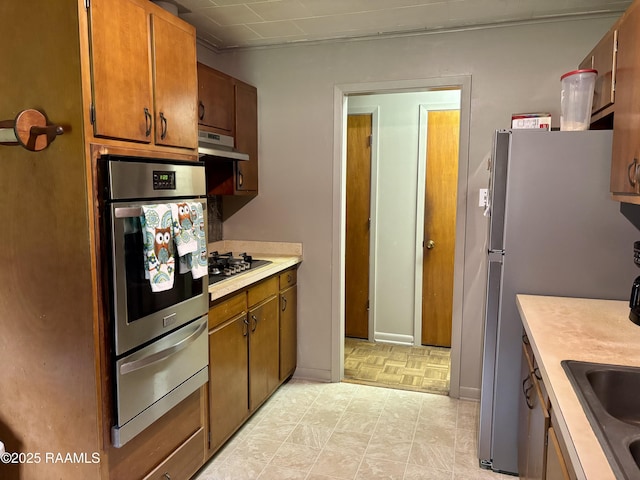 kitchen featuring gas cooktop, light countertops, a warming drawer, under cabinet range hood, and oven