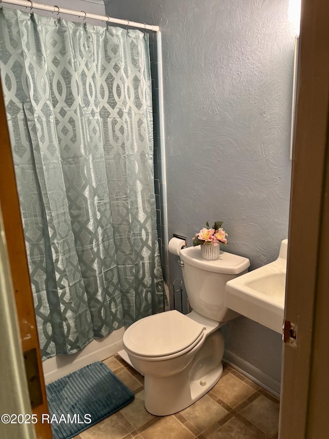 bathroom with tile patterned flooring, a textured wall, shower / bath combo, and toilet