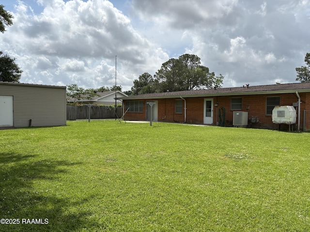 rear view of property featuring fence, central AC unit, a yard, and brick siding