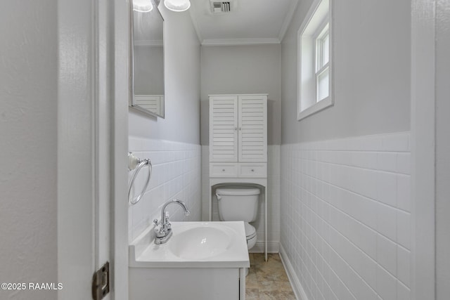 half bathroom with a sink, toilet, tile walls, visible vents, and ornamental molding
