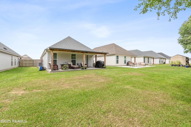 rear view of property with fence, a shingled roof, a lawn, and a patio area