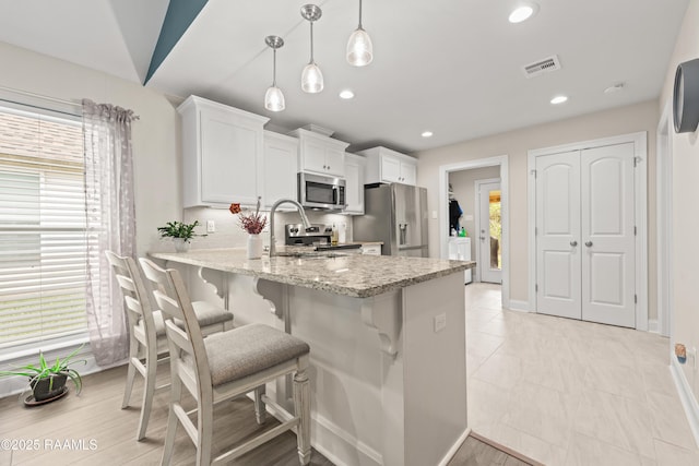 kitchen with light stone counters, stainless steel appliances, white cabinetry, a peninsula, and visible vents