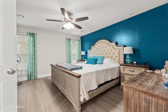 bedroom featuring a ceiling fan, visible vents, multiple windows, and wood finished floors