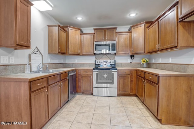kitchen featuring appliances with stainless steel finishes, brown cabinets, a sink, light countertops, and ornamental molding