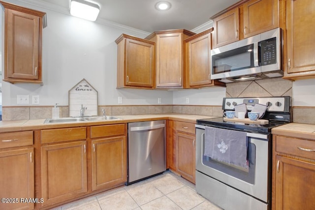 kitchen with crown molding, brown cabinetry, a sink, appliances with stainless steel finishes, and light tile patterned floors